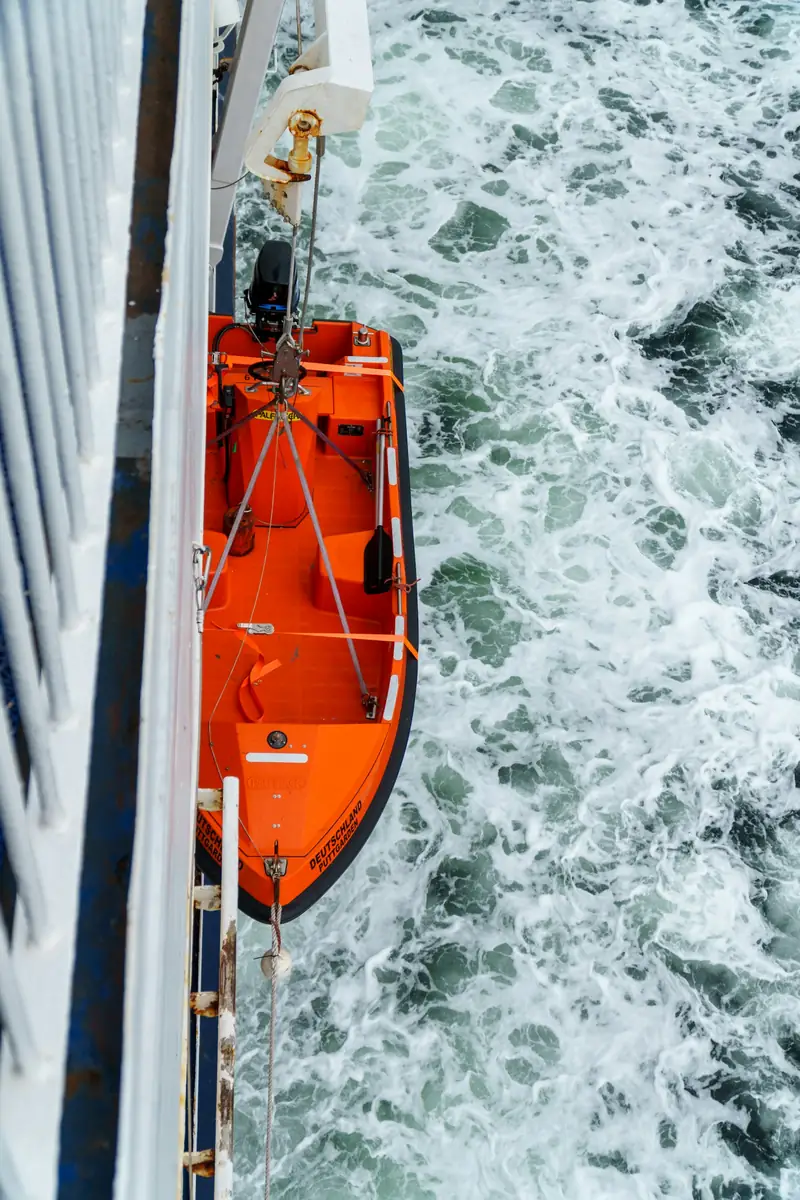 Orange livbåt upphängd över havet vid en färja